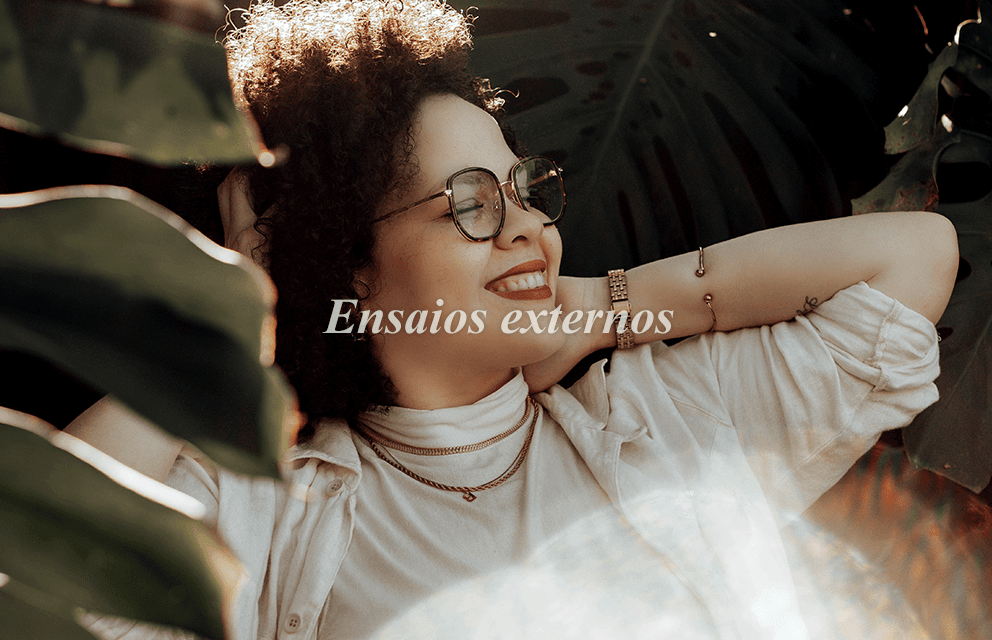 Ensaio fotográfico externo feminino realizado por Fotógrafa Ana. Mulher sorridente de cabelo cacheado e óculos, posando em meio à natureza com iluminação natural.
